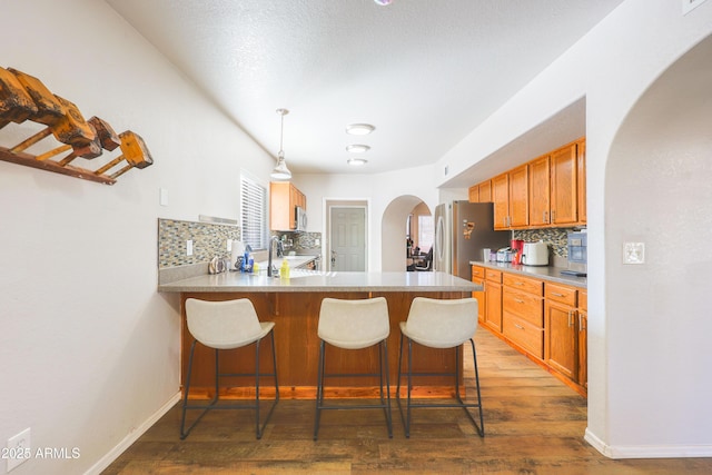 kitchen with appliances with stainless steel finishes, wood-type flooring, a kitchen bar, decorative light fixtures, and kitchen peninsula