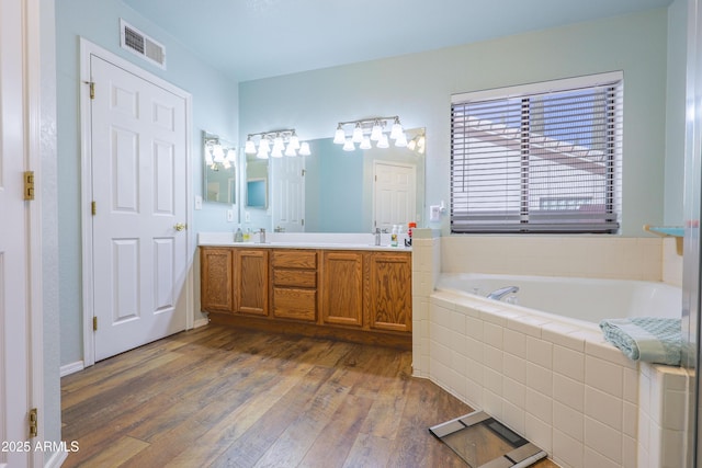 bathroom featuring vanity, tiled tub, and wood-type flooring