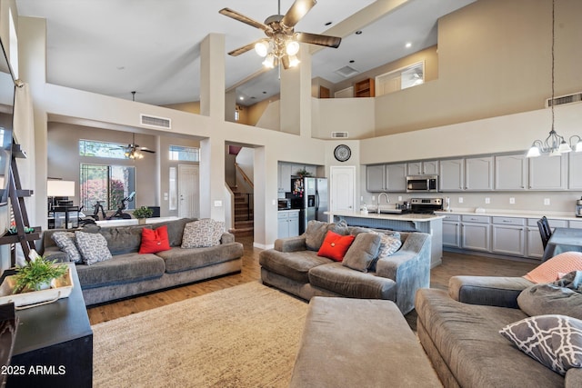 living room featuring dark wood-style floors, visible vents, stairway, and ceiling fan with notable chandelier