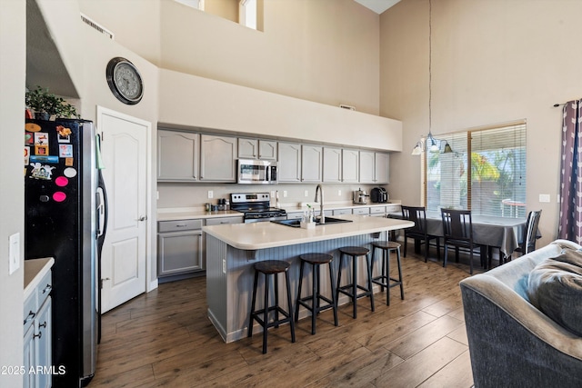 kitchen with a sink, appliances with stainless steel finishes, a kitchen bar, a towering ceiling, and gray cabinets