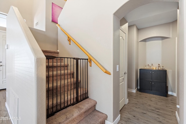 staircase with wood finished floors, visible vents, arched walkways, and baseboards
