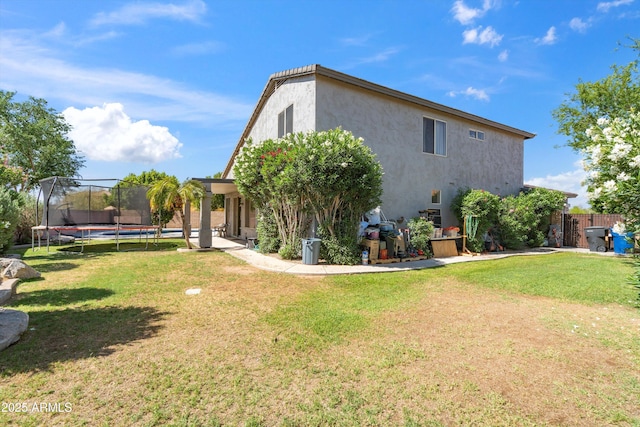 back of property featuring a lawn, a trampoline, and stucco siding