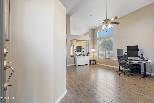 office space featuring a towering ceiling, wood finished floors, a ceiling fan, and baseboards