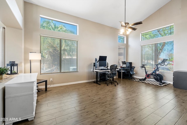 office area with a towering ceiling, wood finished floors, a ceiling fan, and baseboards