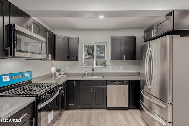 kitchen with light stone countertops, sink, stainless steel appliances, and light hardwood / wood-style floors