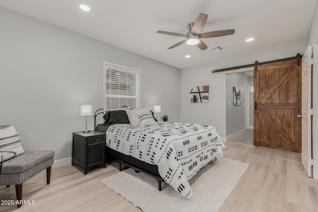 bedroom featuring a barn door, ceiling fan, and light hardwood / wood-style floors