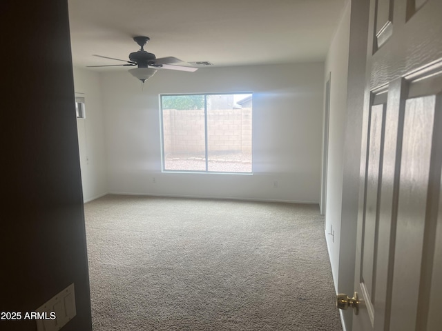 carpeted spare room featuring baseboards, visible vents, and ceiling fan