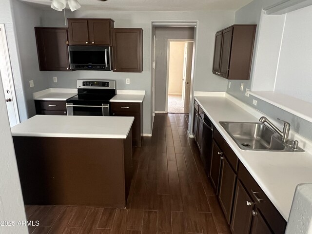 kitchen with dark brown cabinets, a sink, light countertops, appliances with stainless steel finishes, and dark wood-style floors