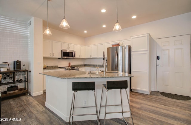 kitchen with dark wood-style flooring, appliances with stainless steel finishes, light stone countertops, white cabinets, and an island with sink