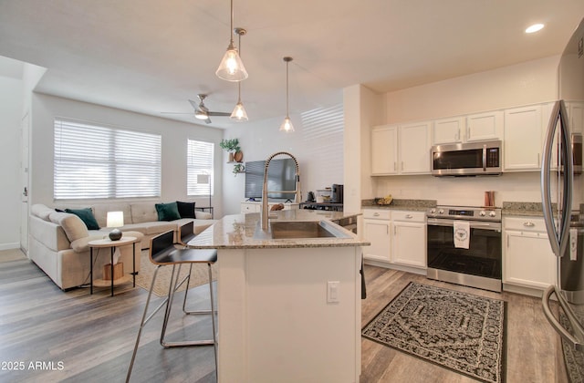 kitchen featuring appliances with stainless steel finishes, white cabinets, light stone countertops, and open floor plan