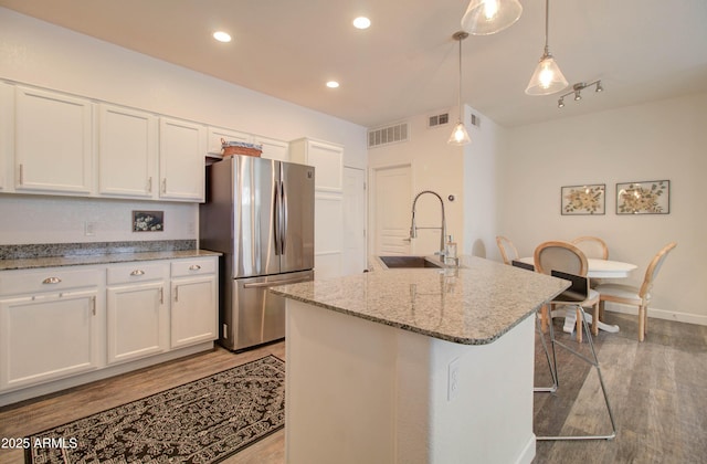 kitchen featuring a sink, freestanding refrigerator, white cabinetry, and visible vents