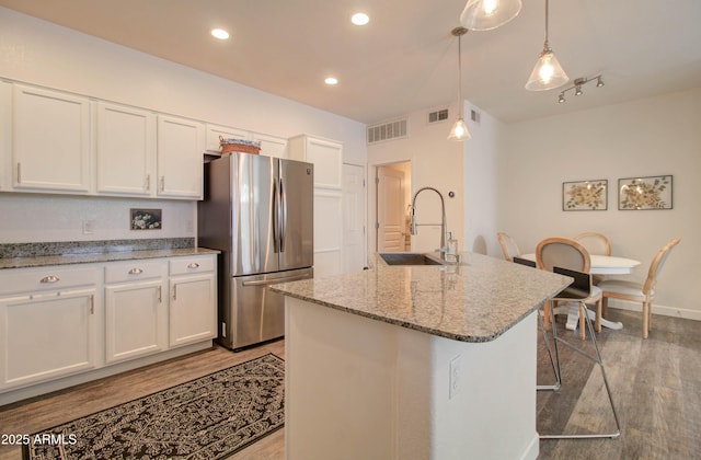 kitchen with freestanding refrigerator, visible vents, a sink, and wood finished floors