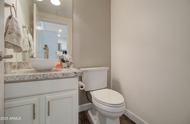 half bath featuring toilet, baseboards, wood finished floors, and vanity