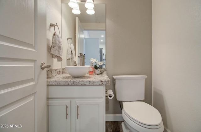 half bath with toilet, baseboards, wood finished floors, and vanity