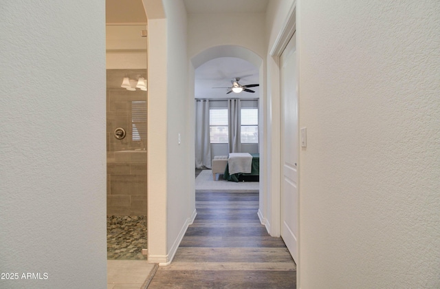 corridor featuring arched walkways, a textured wall, and wood finished floors