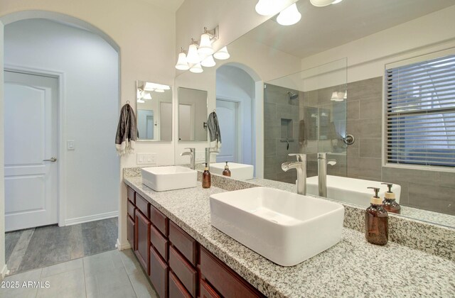 bathroom featuring a sink, tile patterned flooring, double vanity, and tiled shower