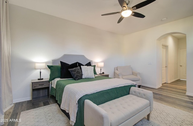 bedroom with arched walkways, baseboards, ceiling fan, and wood finished floors