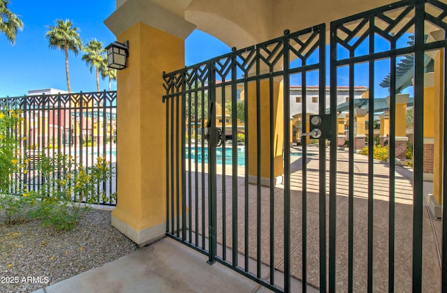 view of gate with a community pool, fence, and a patio area