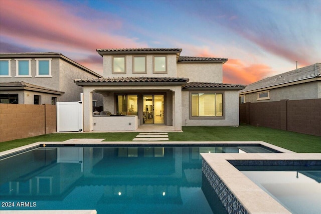 back house at dusk featuring a swimming pool with hot tub, a yard, and a patio area