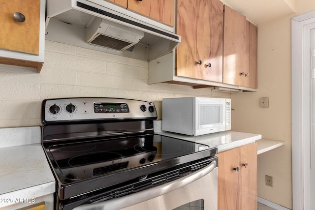 kitchen with under cabinet range hood, stainless steel range with electric stovetop, tasteful backsplash, and light countertops