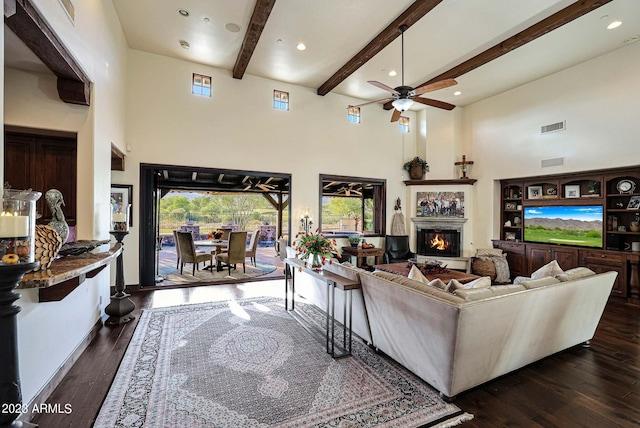 living room with ceiling fan, beamed ceiling, plenty of natural light, and dark hardwood / wood-style flooring