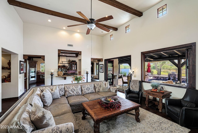 living room with a high ceiling, beam ceiling, ceiling fan, and dark hardwood / wood-style flooring