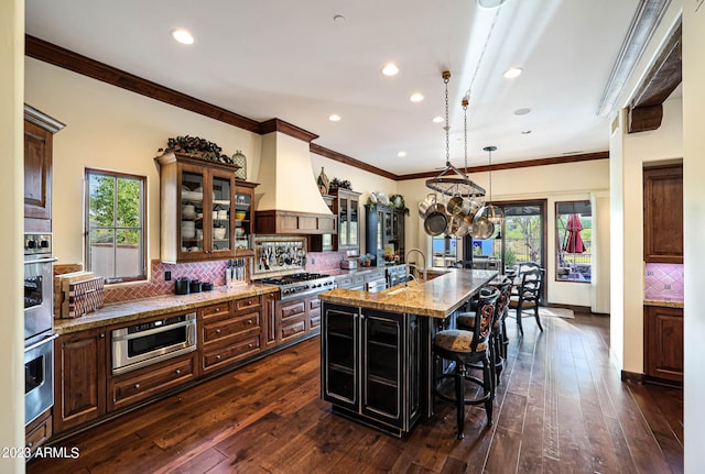 kitchen with an island with sink, custom range hood, light stone countertops, and dark wood-type flooring