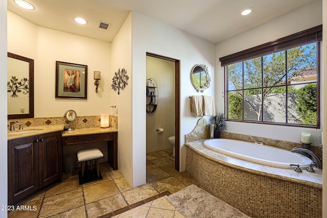 bathroom featuring tiled bath, vanity, and toilet