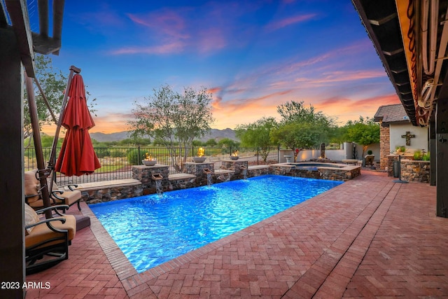 pool at dusk featuring a patio area, a mountain view, an in ground hot tub, and pool water feature