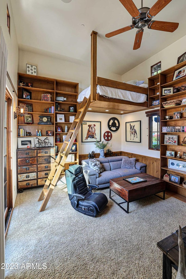 carpeted living room featuring ceiling fan and wooden walls