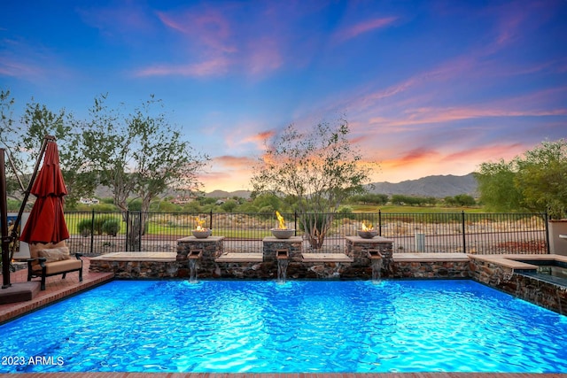 pool at dusk with pool water feature and a mountain view