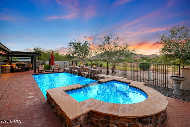 pool at dusk with a patio and an in ground hot tub