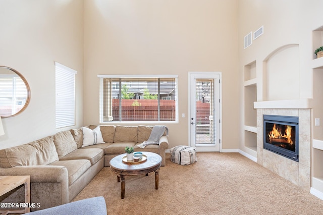 living room with a high ceiling, a tile fireplace, carpet, and built in shelves