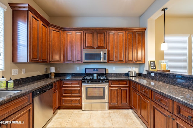 kitchen featuring appliances with stainless steel finishes, hanging light fixtures, dark stone countertops, and light tile patterned floors