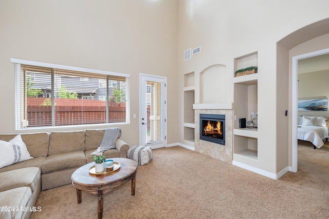 living room with a towering ceiling, a tile fireplace, light carpet, and built in features