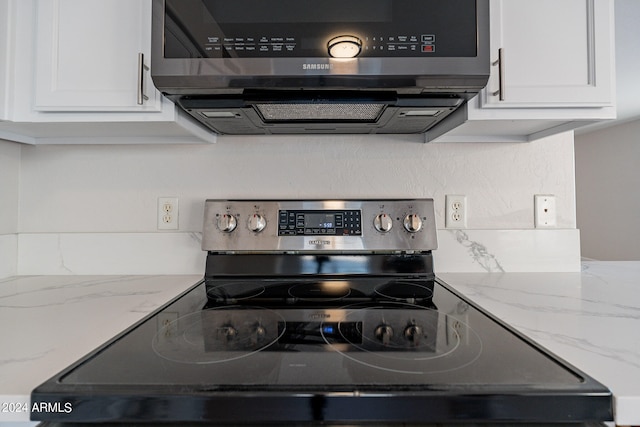 kitchen featuring appliances with stainless steel finishes, white cabinetry, light stone counters, and exhaust hood