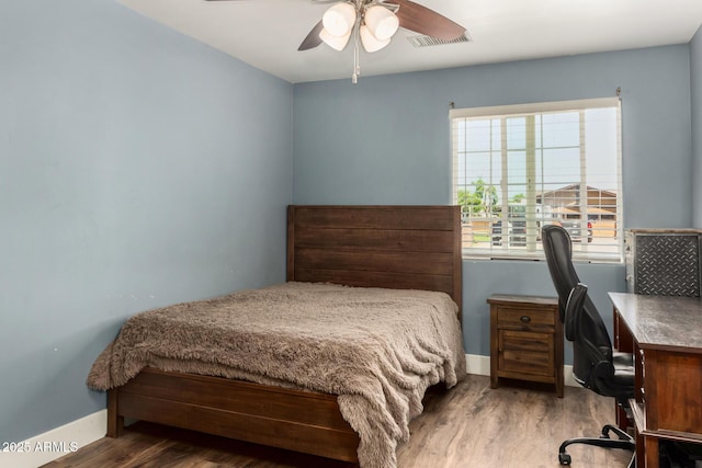 bedroom featuring baseboards, a ceiling fan, wood finished floors, and visible vents