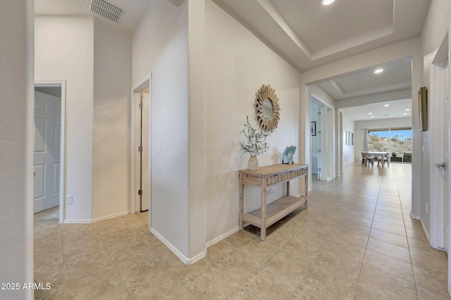 hallway featuring light tile patterned floors, baseboards, visible vents, and a tray ceiling