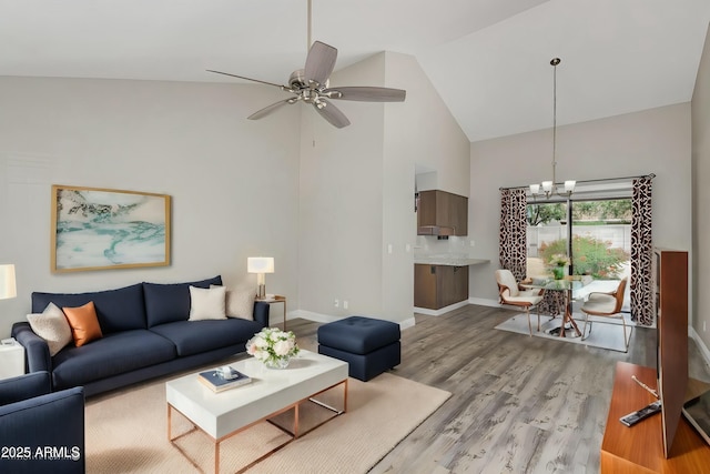 living area with high vaulted ceiling, baseboards, light wood finished floors, and ceiling fan with notable chandelier