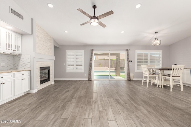 living room with visible vents, a stone fireplace, light wood-style flooring, and ceiling fan with notable chandelier
