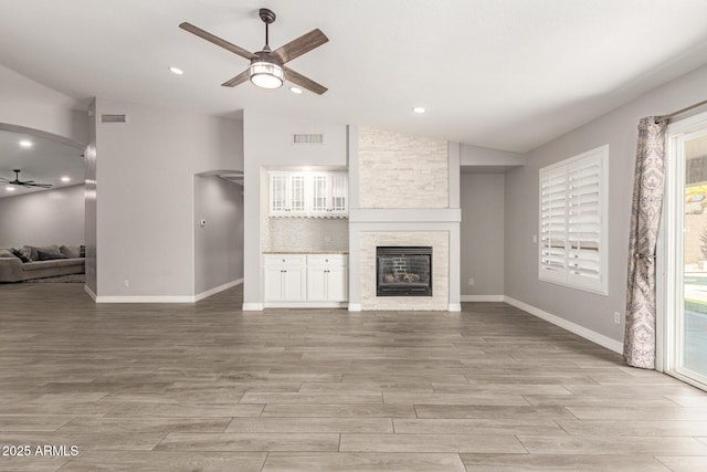 unfurnished living room featuring visible vents, a ceiling fan, vaulted ceiling, and a stone fireplace