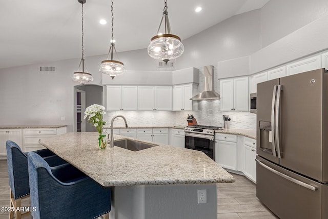 kitchen featuring wall chimney range hood, appliances with stainless steel finishes, a sink, decorative backsplash, and visible vents