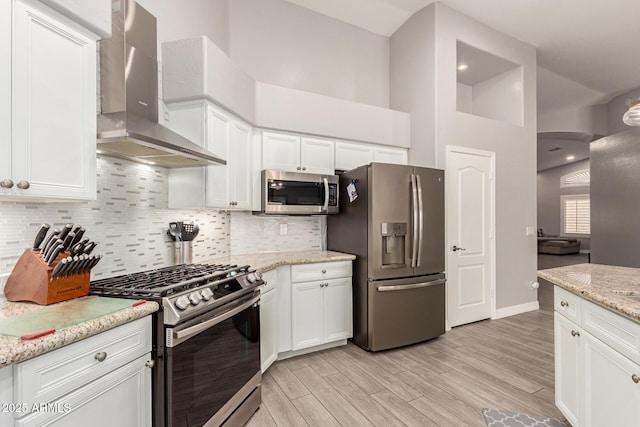 kitchen featuring white cabinets, stainless steel appliances, light wood finished floors, and wall chimney exhaust hood