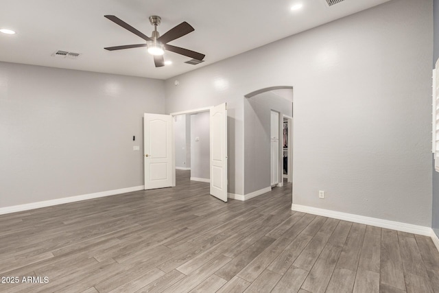 unfurnished room with a ceiling fan, visible vents, arched walkways, wood finished floors, and baseboards