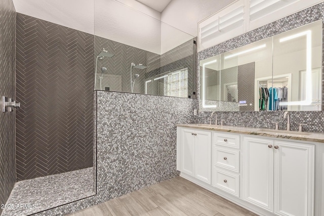 full bath with a sink, a walk in shower, double vanity, and tile walls