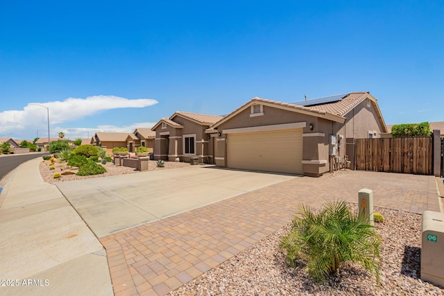 ranch-style home with a garage, fence, stucco siding, roof mounted solar panels, and driveway