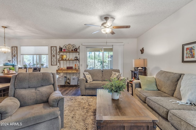 living room with ceiling fan with notable chandelier, wood-type flooring, and a textured ceiling