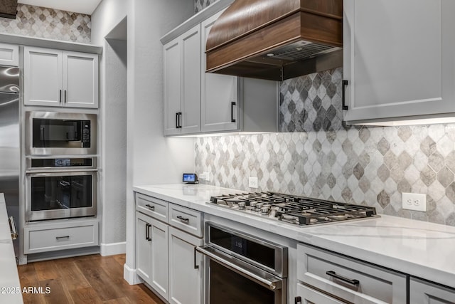 kitchen featuring premium range hood, stainless steel appliances, dark hardwood / wood-style floors, light stone countertops, and decorative backsplash