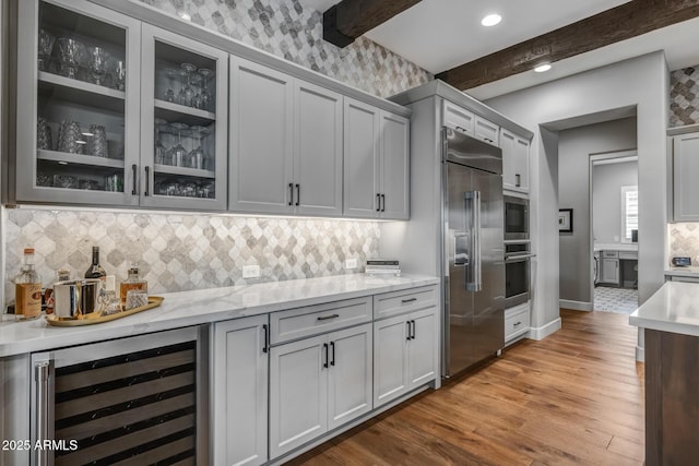 kitchen with beamed ceiling, wine cooler, built in appliances, light stone countertops, and light wood-type flooring