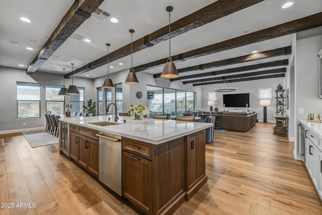 kitchen with sink, dishwasher, light stone countertops, an island with sink, and decorative light fixtures